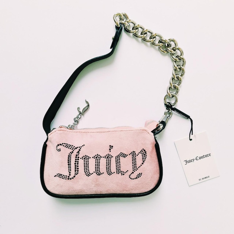 May include: A pink velvet handbag with a black chain strap and the word "Juicy" spelled out in rhinestones. The bag comes with a white tag that reads "Juicy Couture Los Angeles".