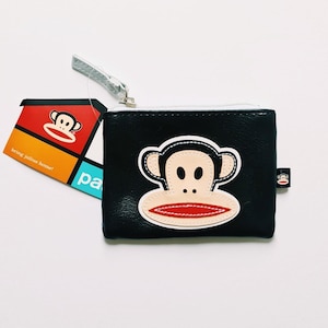 May include: Black leather coin purse with a zipper closure and a large, colorful monkey face applique. The monkey has a red mouth, black eyes, and a white face.