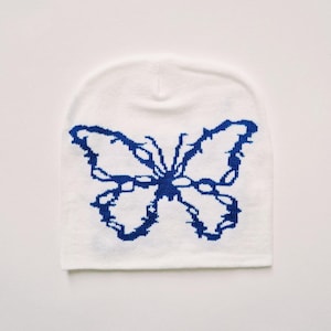 May include: White knitted beanie with a blue butterfly design.