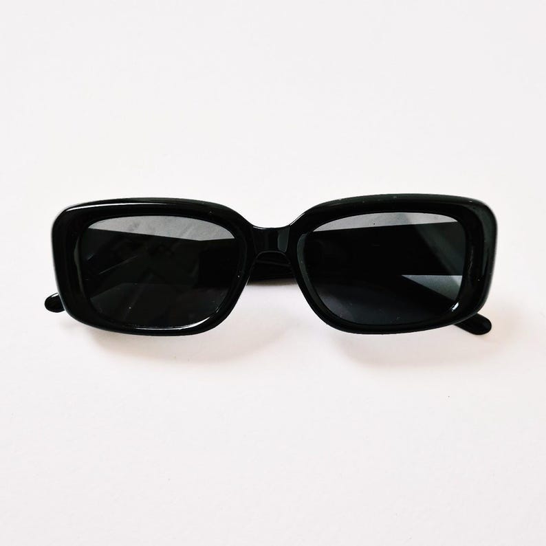 K&ouml;nnte beinhalten: Schwarze quadratische Sonnenbrille mit schwarzen Rahmen und Gl&auml;sern.