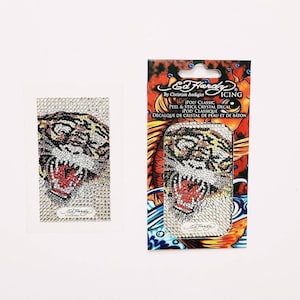 Può includere: Un viso di tigre con un design in cristallo e strass. L'adesivo è per un iPod Classic ed è del marchio Ed Hardy Icing.