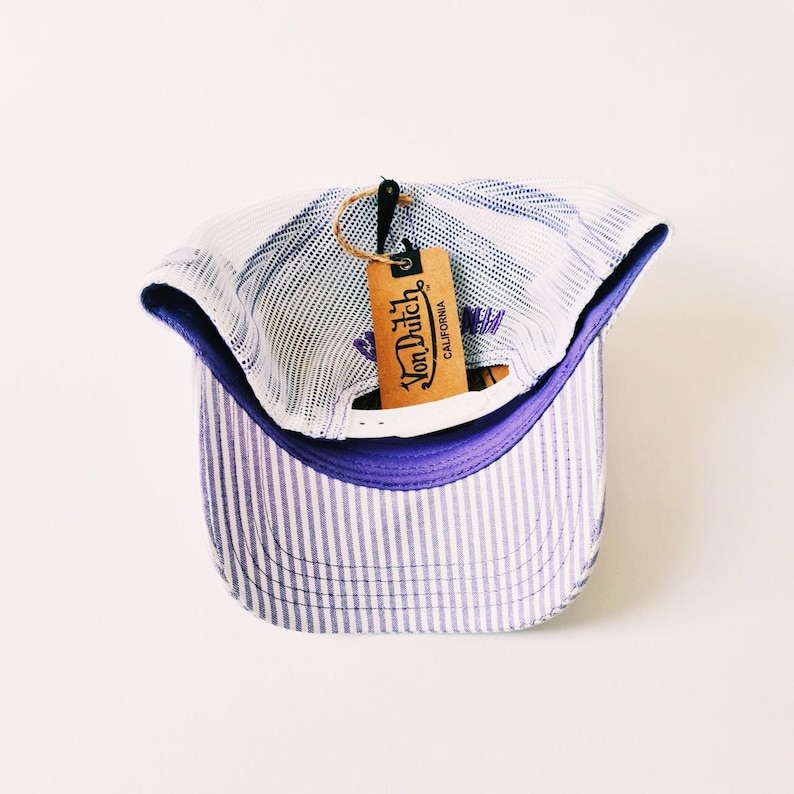 May include: A blue and white striped baseball cap with a mesh back and a purple brim. The cap has a tag that reads "Von Dutch California". The hat is a classic style.