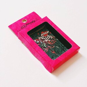 K&ouml;nnte beinhalten: Eine rosa Box mit einem schwarzen und gr&uuml;nen Ed Hardy-Design mit einem Totenkopf, Herzen und den Worten "Love Kills Slowly".