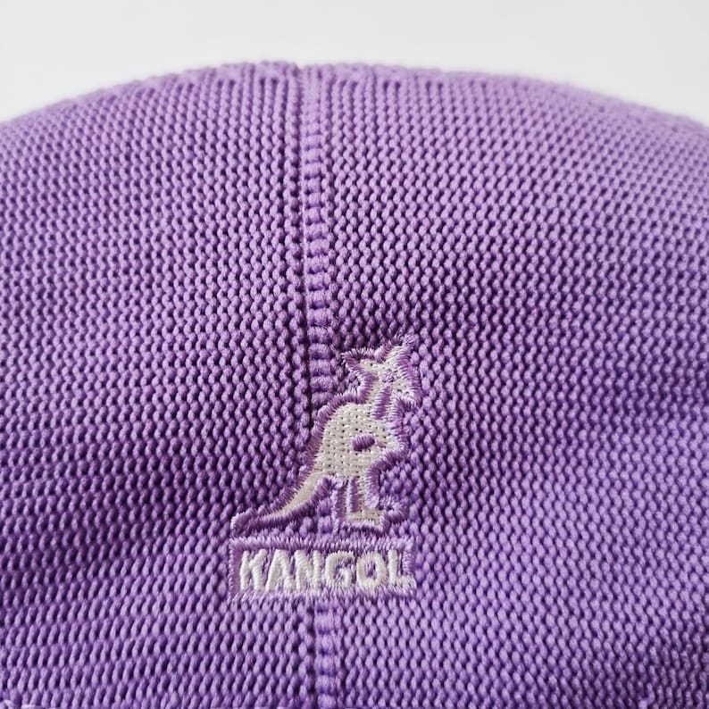 May include: Purple knitted Kangol brand baseball cap with a white embroidered kangaroo logo.