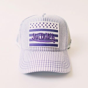 May include: A striped baseball cap with a mesh back. The front features a purple and white patch with the text "Von Dutch" and a star design. The cap has a curved brim and a classic trucker hat style.