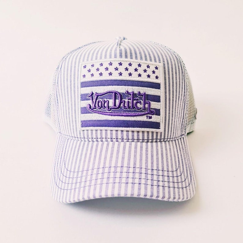 May include: A striped baseball cap with a mesh back. The front features a purple and white patch with the text "Von Dutch" and a star design. The cap has a curved brim and a classic trucker hat style.
