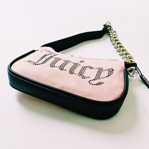 May include: A pink suede handbag with a black trim and a silver chain strap. The bag has the word "Juicy" spelled out in rhinestones.