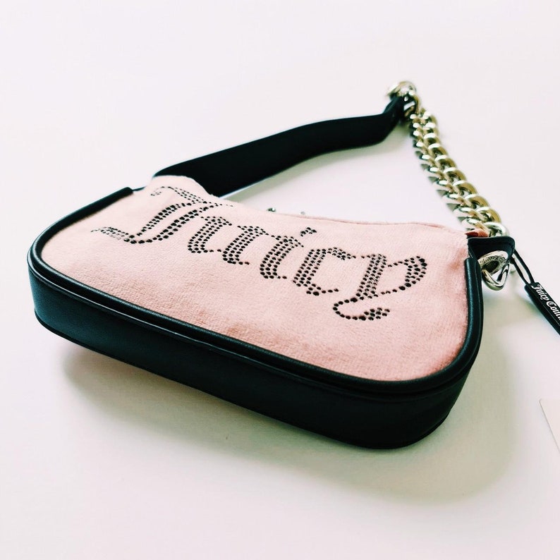 May include: A pink suede handbag with a black trim and a silver chain strap. The bag has the word "Juicy" spelled out in rhinestones.