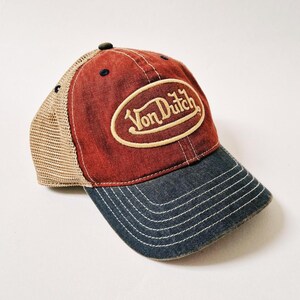 Puede incluir: Gorra de b&eacute;isbol roja, azul y beige con el texto "Von Dutch" en un parche ovalado. La gorra tiene una parte trasera de malla y una visera curva. El sombrero est&aacute; hecho de mezclilla y lona.