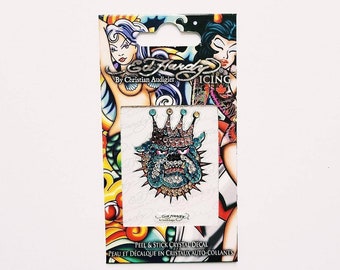 May include: A sticker featuring a cartoon bulldog wearing a jeweled crown. The sticker is on a white background with the text "Ed Hardy" and "ICING" on the packaging. The sticker is a peel and stick crystal decal.