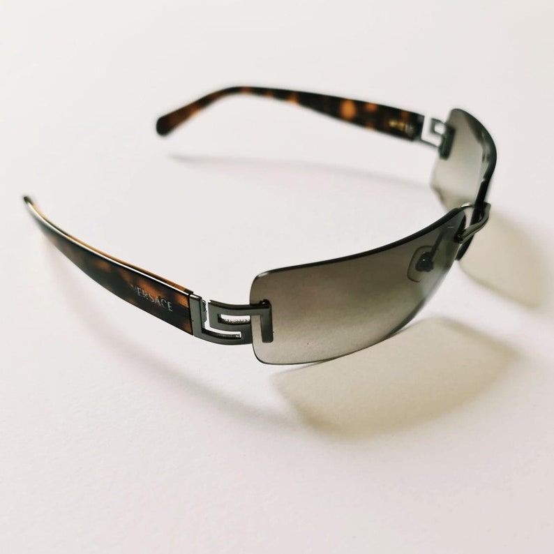 May include: Brown and black tortoiseshell sunglasses with a silver frame and gray lenses. The sunglasses have the word "VERSACE" written on the side.
