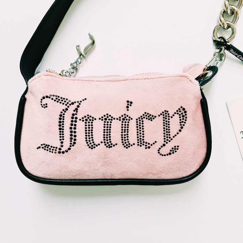 May include: A pink velvet handbag with a black strap and a silver chain. The bag has the word "Juicy" spelled out in black rhinestones.