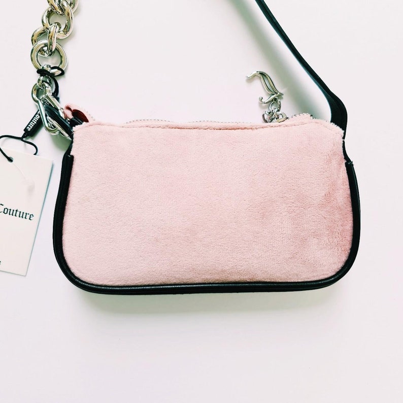 May include: A pink velvet handbag with a black leather trim and a silver chain strap. The bag has a small silver charm attached to the zipper.
