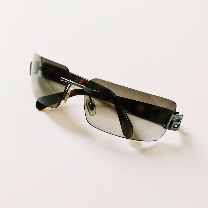 May include: A pair of black sunglasses with a brown tortoise shell frame and gray lenses. The sunglasses have a square shape and a metal accent on the side.