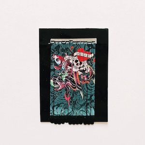 K&ouml;nnte beinhalten: Ein Satz schwarzer Haarklammern mit einem bunten Design, das einen Totenkopf, ein Herz und ein Banner mit der Aufschrift "Love Kills Slowly" zeigt.