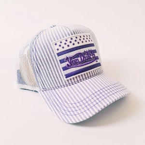 May include: A baseball cap with a striped pattern and a mesh back. The cap has a purple and white striped design and a rectangular patch with the text "Von Dutch" in purple. The patch also features a stars and stripes design.