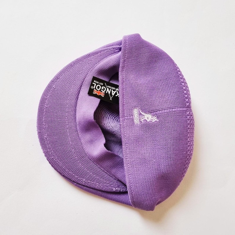 May include: A purple knitted Kangol brand cap with a kangaroo logo on the side. The cap is folded in half and the Kangol logo is visible on the inside of the cap.