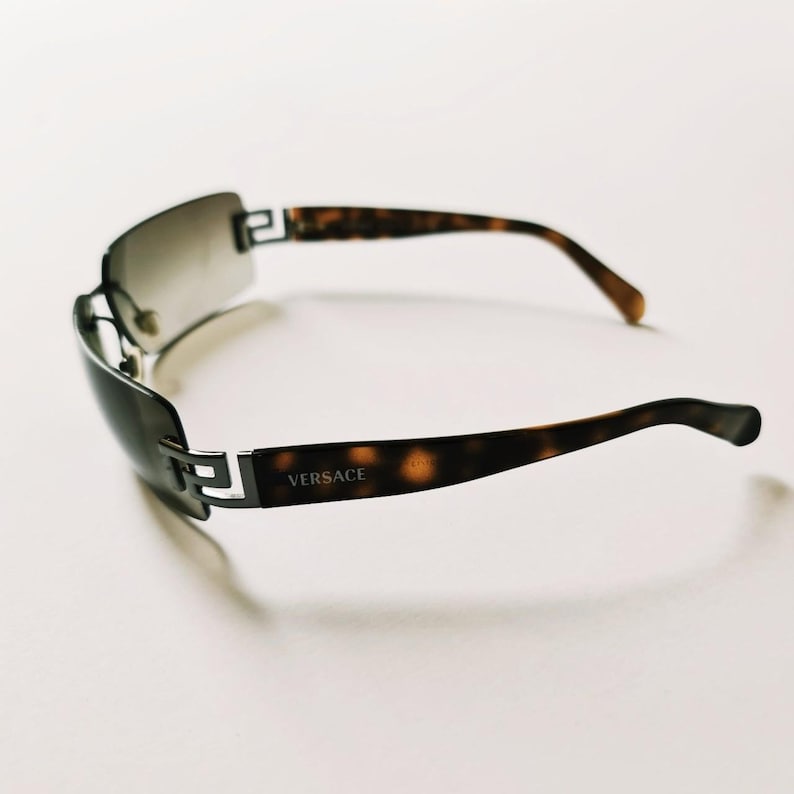 May include: A pair of brown and black tortoiseshell sunglasses with a silver frame and the word "VERSACE" printed on the frame.