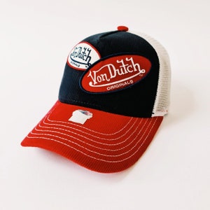 May include: A red, white, and blue trucker hat with a navy blue crown and a red bill. The hat has a white mesh back and features a large "Von Dutch Originals" logo in red and white on the front.
