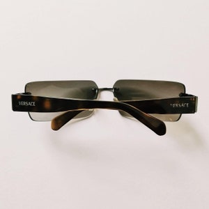 May include: Brown and black square-shaped sunglasses with the word "VERSACE" on each arm.