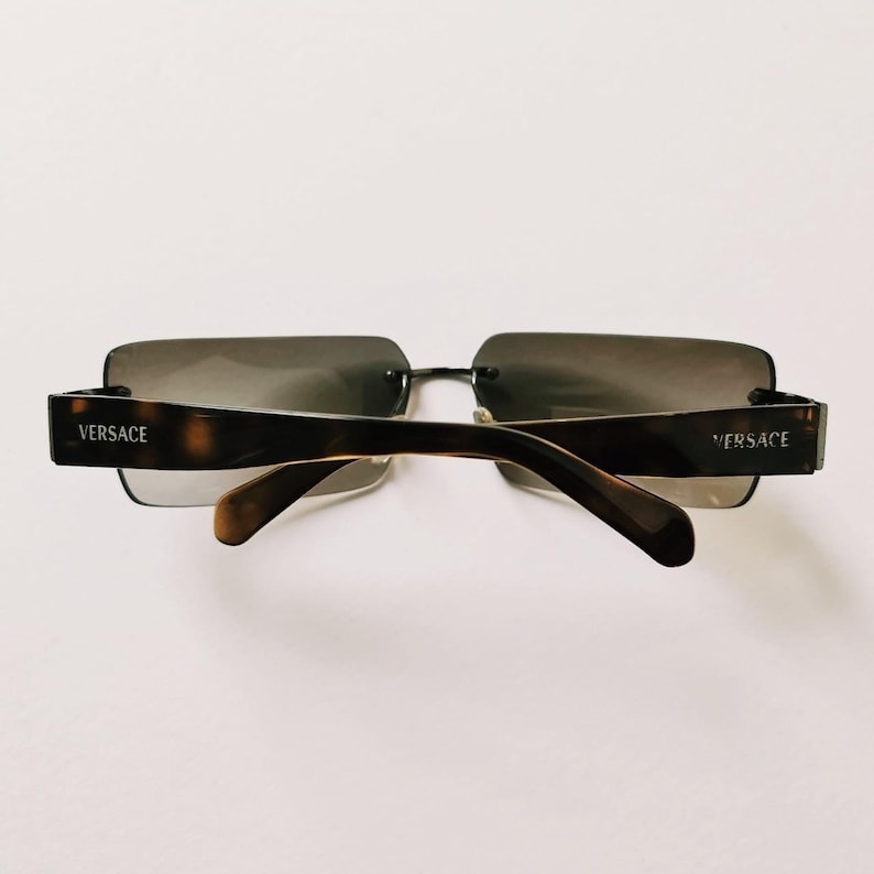 May include: Brown and black square-shaped sunglasses with the word "VERSACE" on each arm.