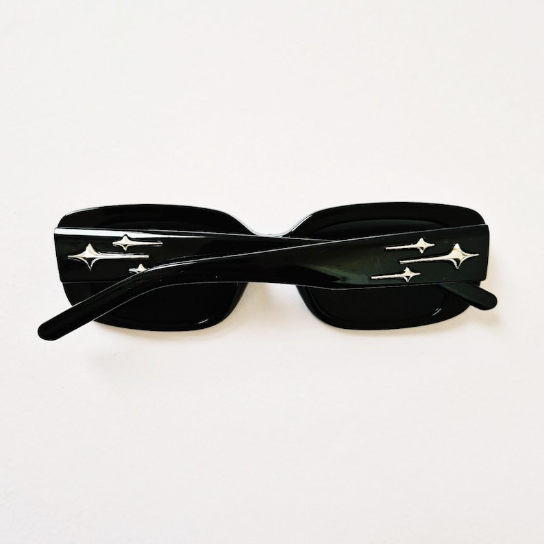 K&ouml;nnte beinhalten: Schwarze quadratische Sonnenbrille mit silbernen Stern-Akzenten an den B&uuml;geln.