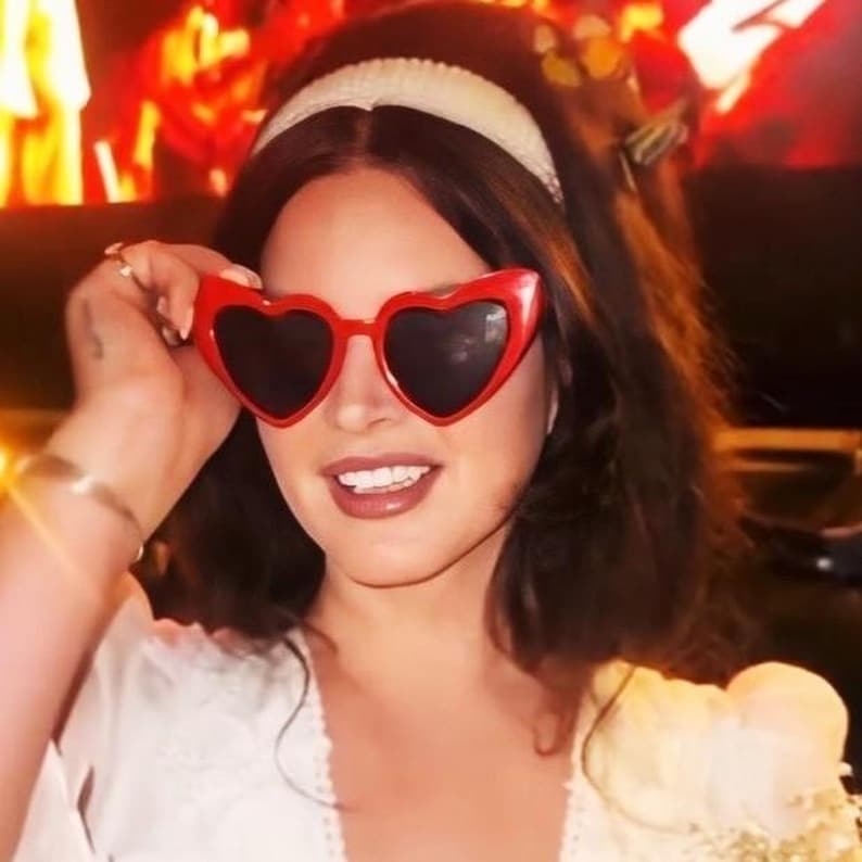 May include: A woman wearing a white headband and red heart-shaped sunglasses. She is smiling and looking at the camera.