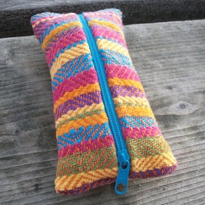 Könnte beinhalten: Eine farbenfrohe Reißverschlusstasche mit einem Außenmaterial aus gewebtem Stoff. Die Tasche hat einen blauen Reißverschluss und ist aus verschiedenen Farben gefertigt, darunter Pink, Orange, Gelb und Grün.