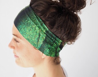 Puede incluir: Una diadema ancha de tela con un vibrante patrón digital de matriz en verde y negro. El accesorio está confeccionado con un material liso y flexible que envuelve la cabeza, mostrando un diseño repetitivo de flujo de datos vertical.