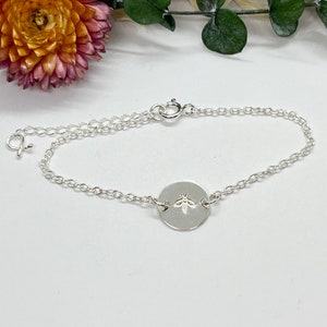 May include: A silver chain bracelet with a small round charm featuring a bee design.