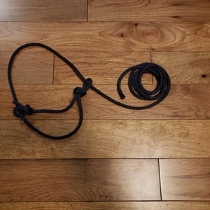 May include: A black rope with two knots tied in it. The rope is laid out on a wooden floor with a coil of the same rope to the right.