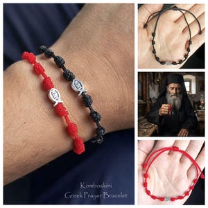 May include: Two knotted cord bracelets in red and black, each featuring a silver-toned fish charm with the word Jesus inscribed. The bracelets have adjustable sliding knots and are labelled as Komboskini Greek Prayer Bracelets.