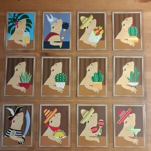 以下が含まれることがあります： 様々な帽子をかぶり、様々な物を手にしたヒゲトカゲを描いたイラストカード10枚セット。カードはすべて同じようなスタイルで、茶色の背景に白い縁取りが施されています。ヒゲトカゲはそれぞれ異なる帽子をかぶっており、中にはソンブレロ、海賊帽、カウボーイハットなどがあります。また、サボテン、マラカス、テキーラのボトルなど、様々な物を手にしています。