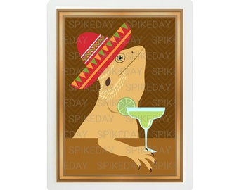 Peut inclure: Un lézard barbu portant un sombrero rouge, jaune et vert et tenant un verre de margarita avec un quartier de citron vert. L'image est encadrée dans un cadre doré sur un fond brun.