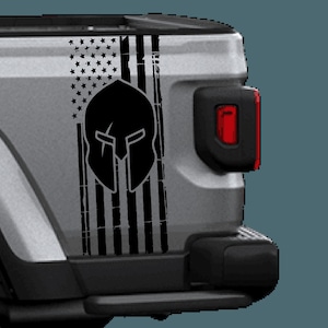 May include: A black and white distressed American flag decal with a Spartan helmet graphic. The decal is applied to the tailgate of a silver pickup truck.