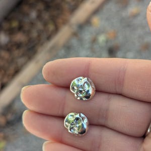 May include: A pair of silver skull stud earrings. The skulls are textured and have a slightly rough finish.