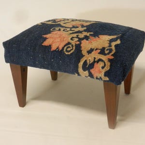 May include: A blue and beige patterned footstool with wooden legs.