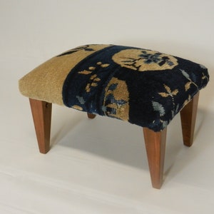 May include: A small, rectangular footstool with four wooden legs. The top is upholstered in a blue and beige patterned fabric.