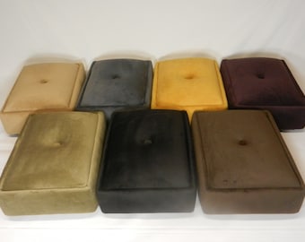 May include: A collection of seven rectangular, upholstered footstools in various colors, including beige, gray, yellow, burgundy, olive green, black, and brown. Each stool features a button in the center of the top surface.