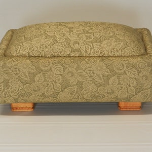 May include: A rectangular footstool with a floral patterned fabric upholstery and wooden legs.