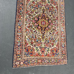 May include: Rectangular Persian rug with a cream-colored field and a detailed floral pattern in shades of red, blue, green, and gold. The rug has a dark blue border and intricate design.