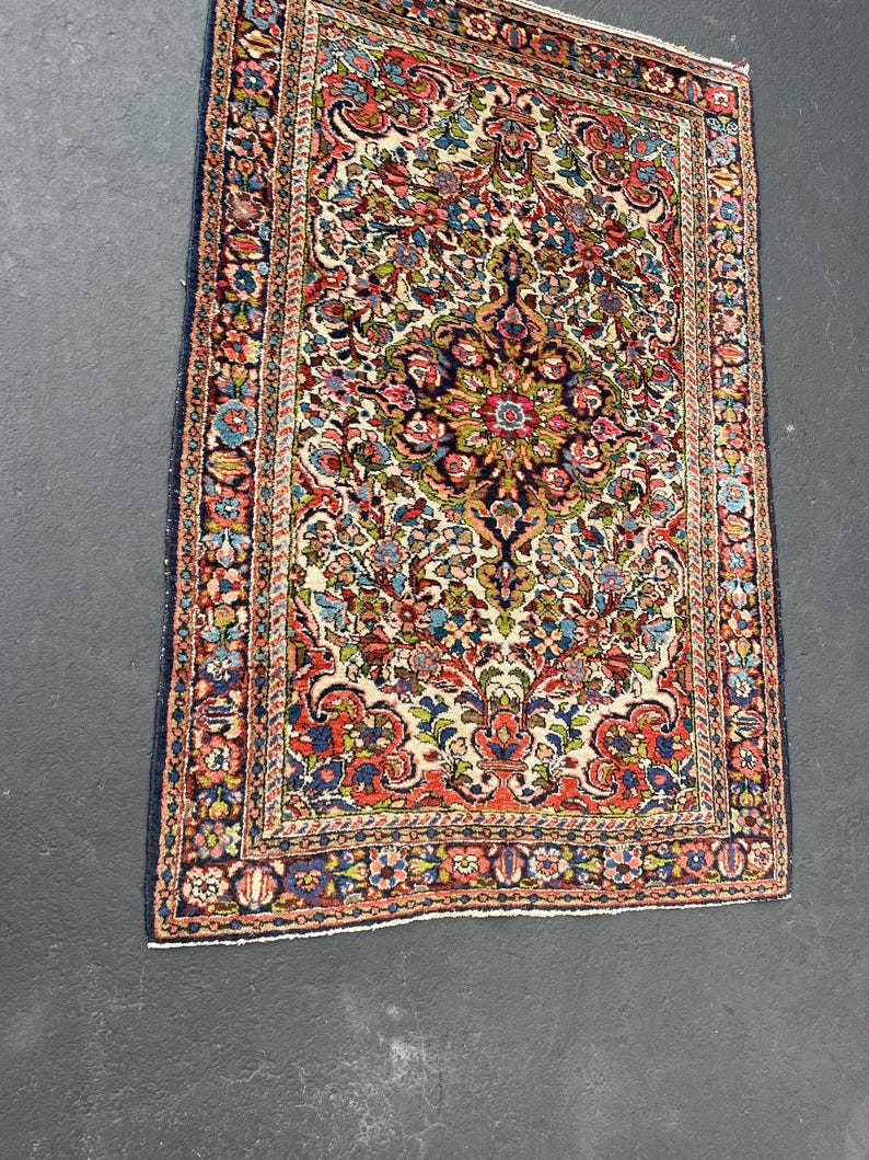May include: Rectangular Persian rug with a cream-colored field and a detailed floral pattern in shades of red, blue, green, and gold. The rug has a dark blue border and intricate design.