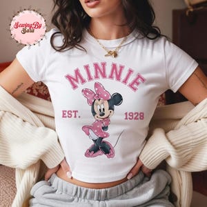 A woman wearing a white t-shirt with a Minnie Mouse graphic and text, along with a necklace.