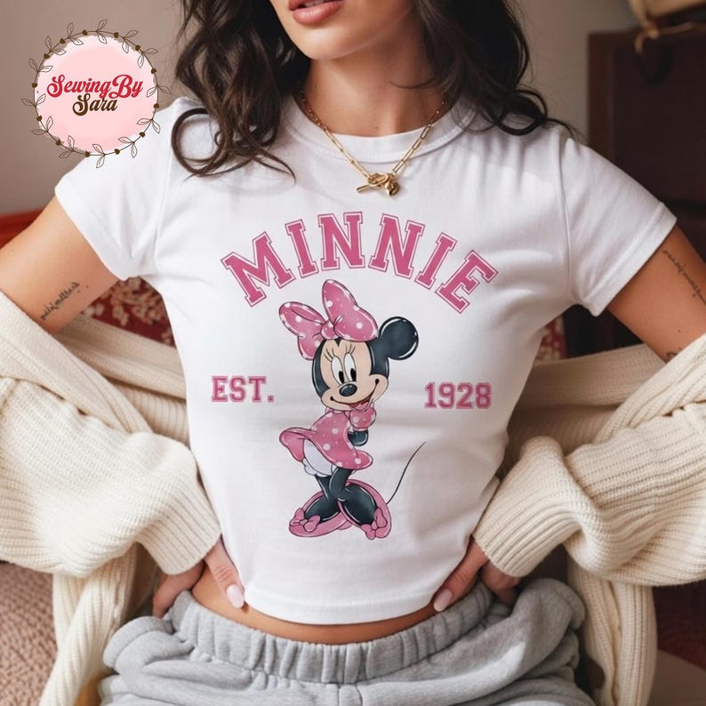 A woman wearing a white t-shirt with a Minnie Mouse graphic and text, along with a necklace.