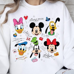 A white sweatshirt with various Disney characters and their signatures printed on it.