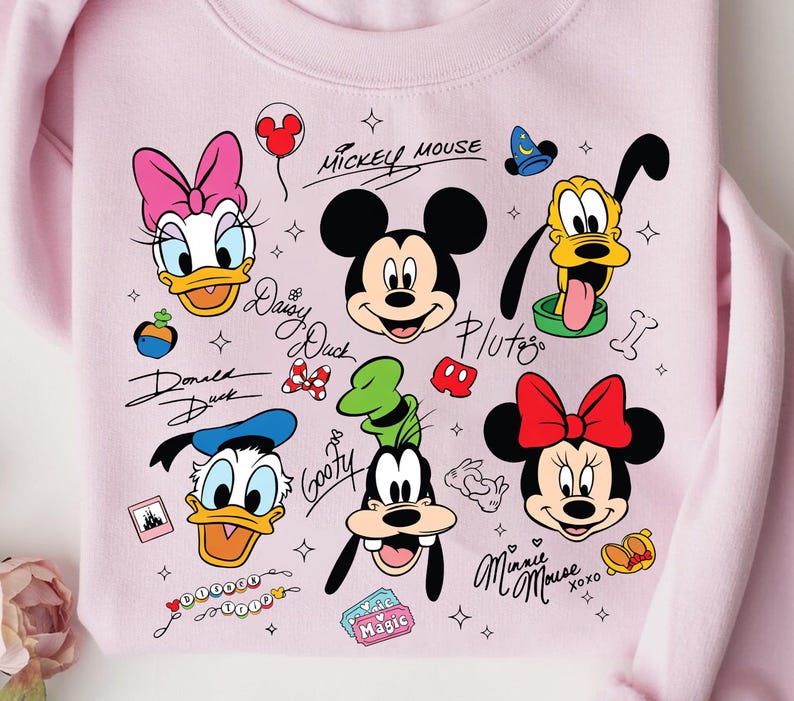 A pink sweatshirt with various Disney characters and logos printed on it, including Mickey Mouse, Donald Duck, Goofy, Minnie Mouse, and Pluto.