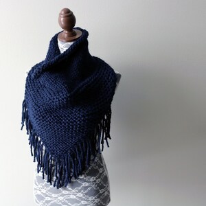 May include: A navy blue knitted scarf with fringe on the edges. The scarf is draped over a mannequin.
