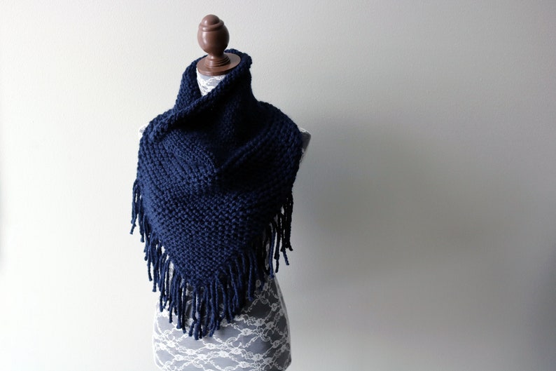 May include: A navy blue knitted scarf with fringe on the edges. The scarf is draped over a mannequin.