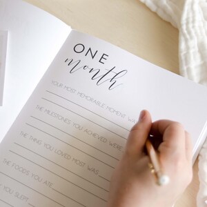 May include: A white page with black text that reads 'ONE month' and has prompts for writing about a baby's first month. The prompts include 'Your most memorable moment was', 'The milestones you achieved were', 'The thing you loved most was', 'The foods you ate', and 'How you slept'.