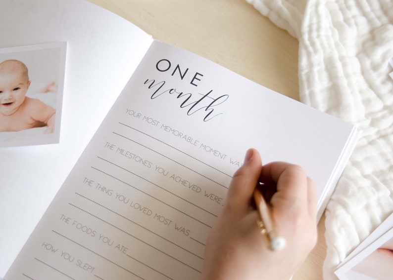 May include: A white page with black text that reads 'ONE month' and has prompts for writing about a baby's first month. The prompts include 'Your most memorable moment was', 'The milestones you achieved were', 'The thing you loved most was', 'The foods you ate', and 'How you slept'.